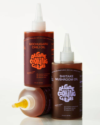 Close-up of Gochugaru Chili Oil and Shiitake Mushroom Oil bottles showing dark infused oils with white squeeze caps