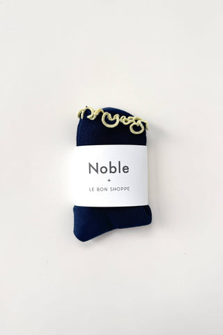 Legs wearing cream-colored ribbed socks with navy ruffled trim detail photographed from above on metal grating