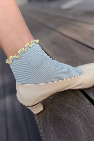 Close-up of light blue ruffled modal sock worn with cream low heel pump showing wavy trim detail at ankle