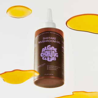 Single bottle of Shiitake Mushroom Oil with golden oil droplets floating beside it on white background