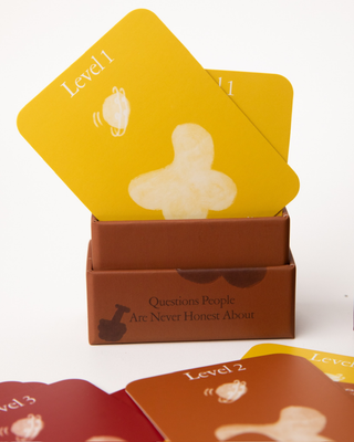 Yellow Level 1 cards emerging from open rust-colored box of Questions People Are Never Honest About conversation game