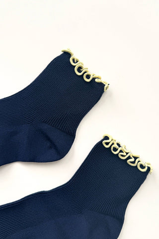 Navy blue petite ruffled modal socks with cream trim folded and wrapped in Noble Le Bon Shoppe branded paper