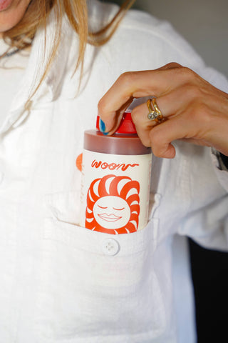 Hand holding Woon Mama's Way hot sauce bottle showing red squeeze top cap up close